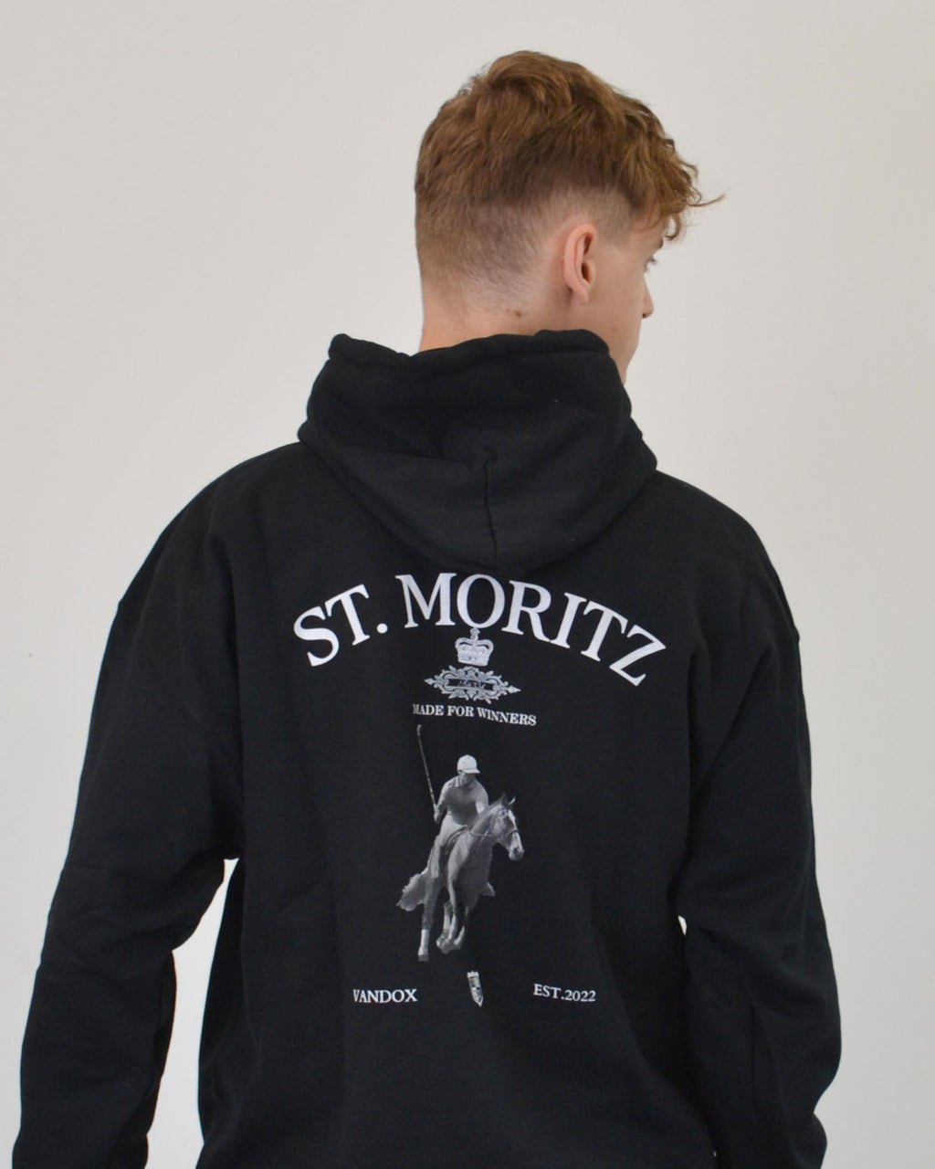 Male model wearing the Polo Club Hoodie in black by Vandox - a luxury oversized hoodie featuring a bold “St. Moritz” graphic and a polo player motif. Designed for those who embody confidence and sophistication, this piece merges elite sport heritage with refined streetwear aesthetics. Starboy old money hoodie sweatshirt clothes vandox sacrevandox vandox clothes vandox clothing