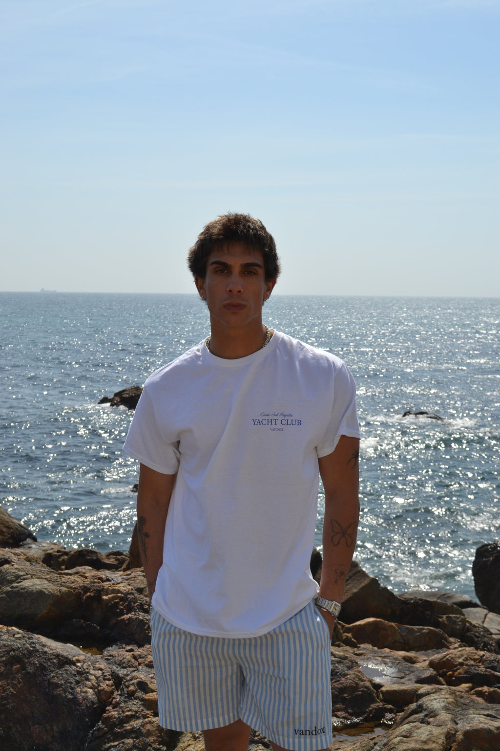 Person wearing a white shirt with text standing on rocks by the water

White
