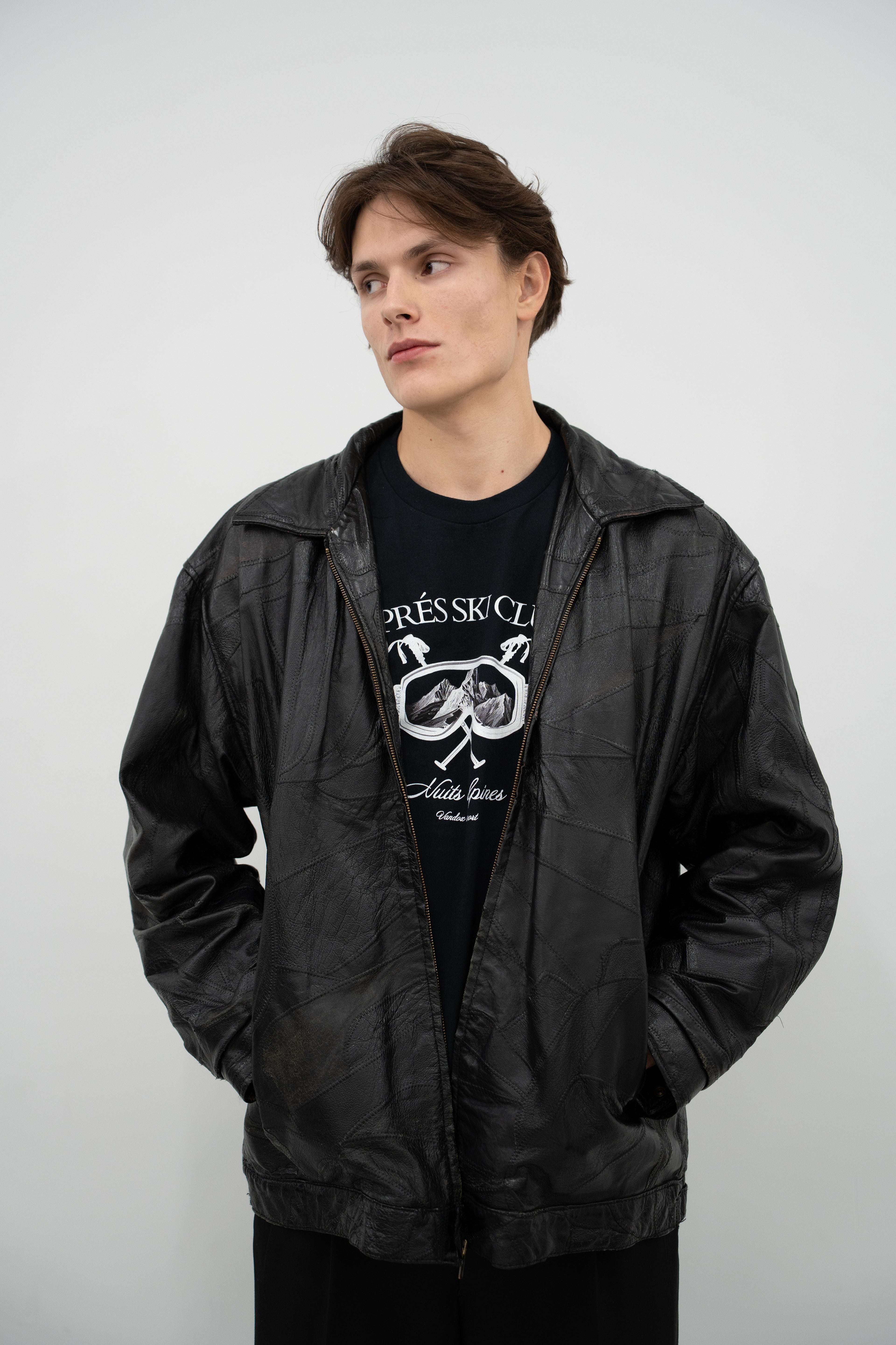 Model wearing deep black Vandox Ski Society T-Shirt with alpine ski goggle graphic and “Après Ski Club” text, styled with leather jacket in luxury starboy old money aesthetic from Vandox clothing collection