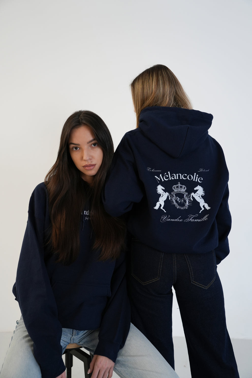 Two models wearing Navy Vandox Mélancolie Hoodie with regal crest, horses graphic and “Mélancolie – Vandox Famille” text on the back, luxury starboy old money aesthetic hoodie from Vandox clothing collection