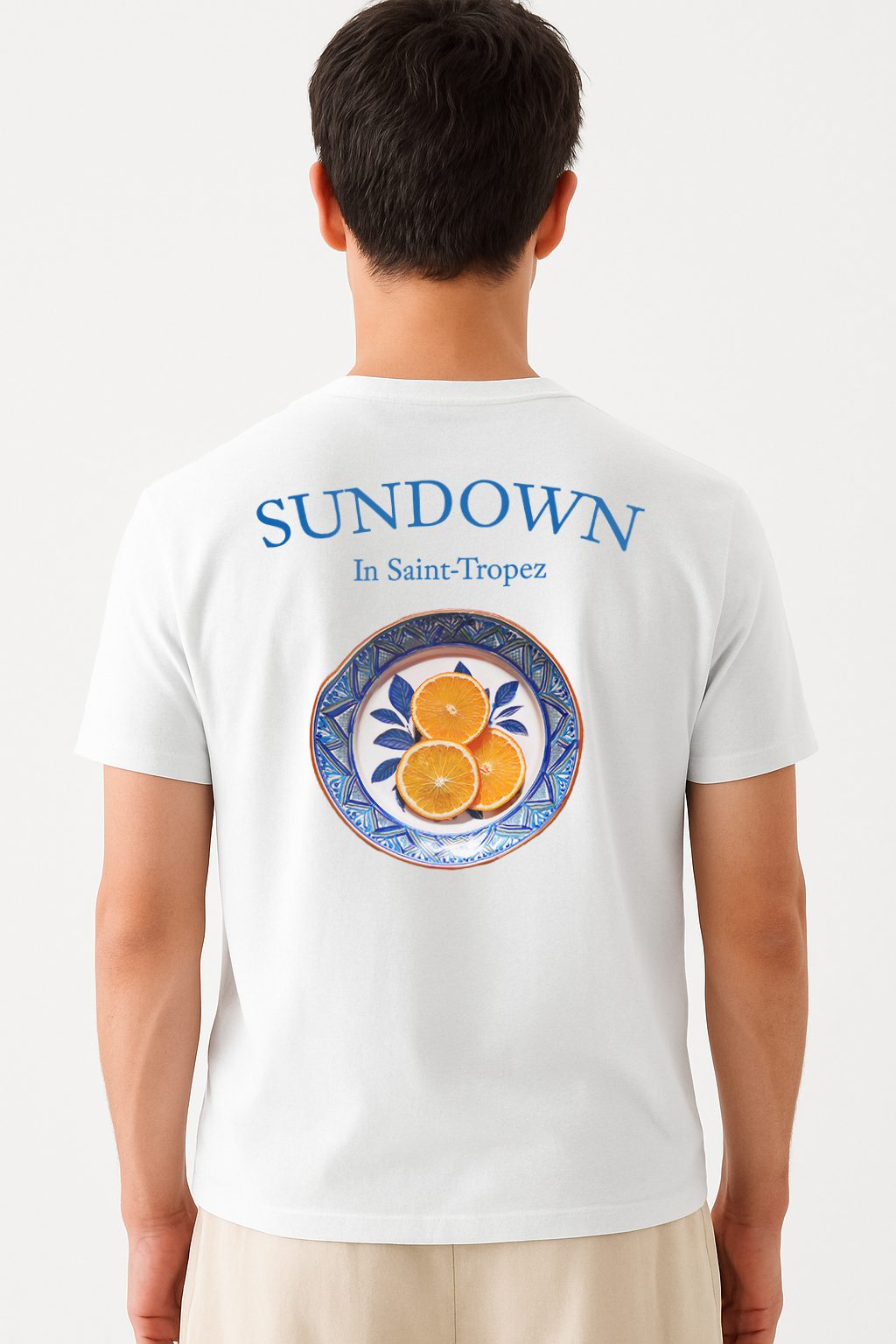 Model wearing the Eggshell White Citrus Sunset T-Shirt by Vandox, featuring a hand-painted style plate of oranges with "Sundown in Saint-Tropez" printed above for a bold Riviera-inspired aesthetic.