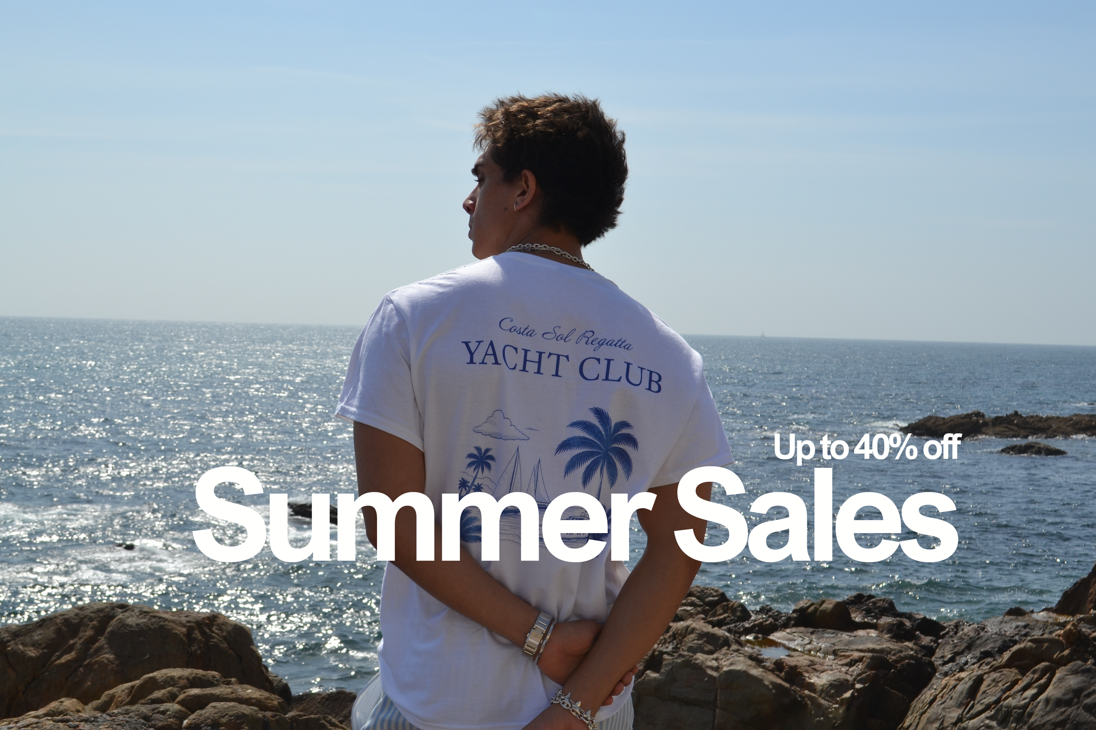 A man stands on rocky shore looking out at the ocean under a clear sky, wearing a white vandox riviera regatta T-shirt with blue text reading 'Cruis and Regatta YACHT CLUB' and palm tree graphics. Large overlaid text says 'Summer Sales' and 'Up to 40% off'.