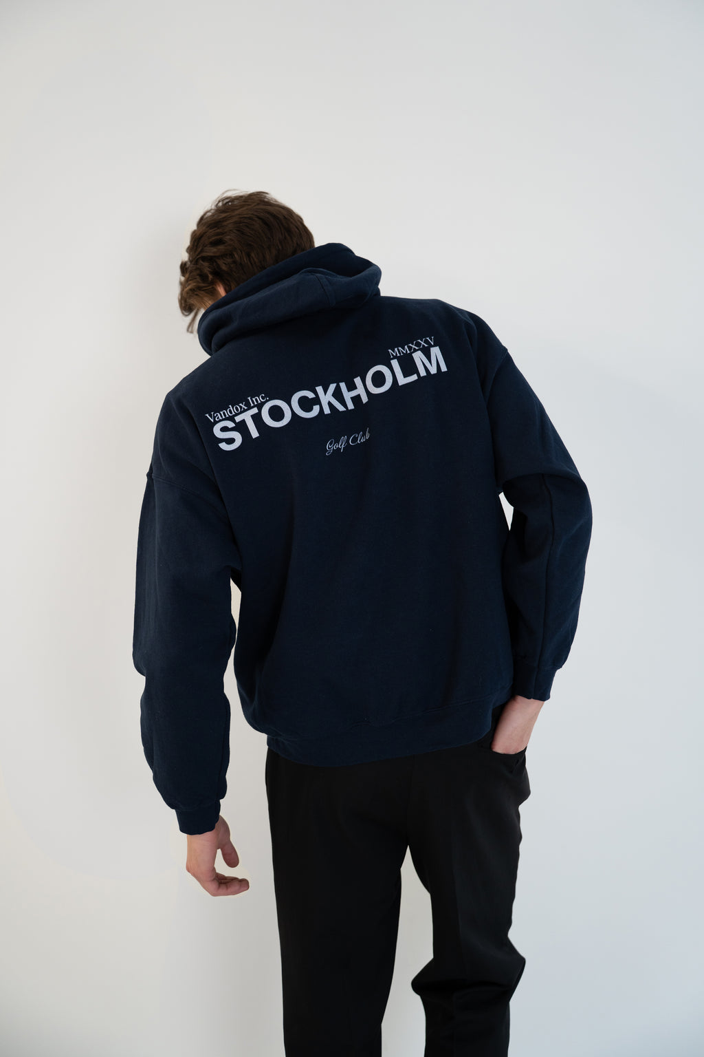 Back view of model wearing Deep Navy Blue Vandox Stockholm Hoodie with “Vandox Inc.” and bold “STOCKHOLM” lettering and Golf Club detail, luxury starboy old money aesthetic hoodie from Vandox clothing collection