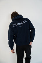 Back view of model wearing Deep Navy Blue Vandox Stockholm Hoodie with “Vandox Inc.” and bold “STOCKHOLM” lettering and Golf Club detail, luxury starboy old money aesthetic hoodie from Vandox clothing collection